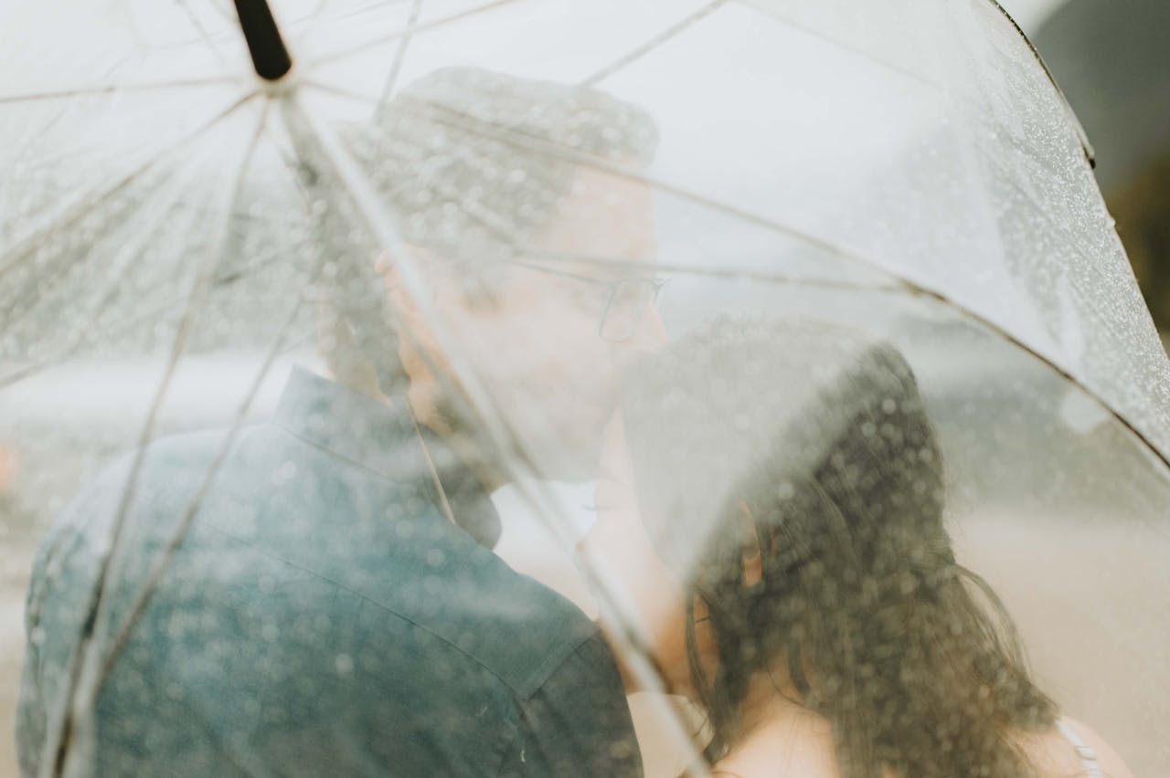 A romantic moment of a couple kissing under an umbrella in the rain, capturing love and intimacy.