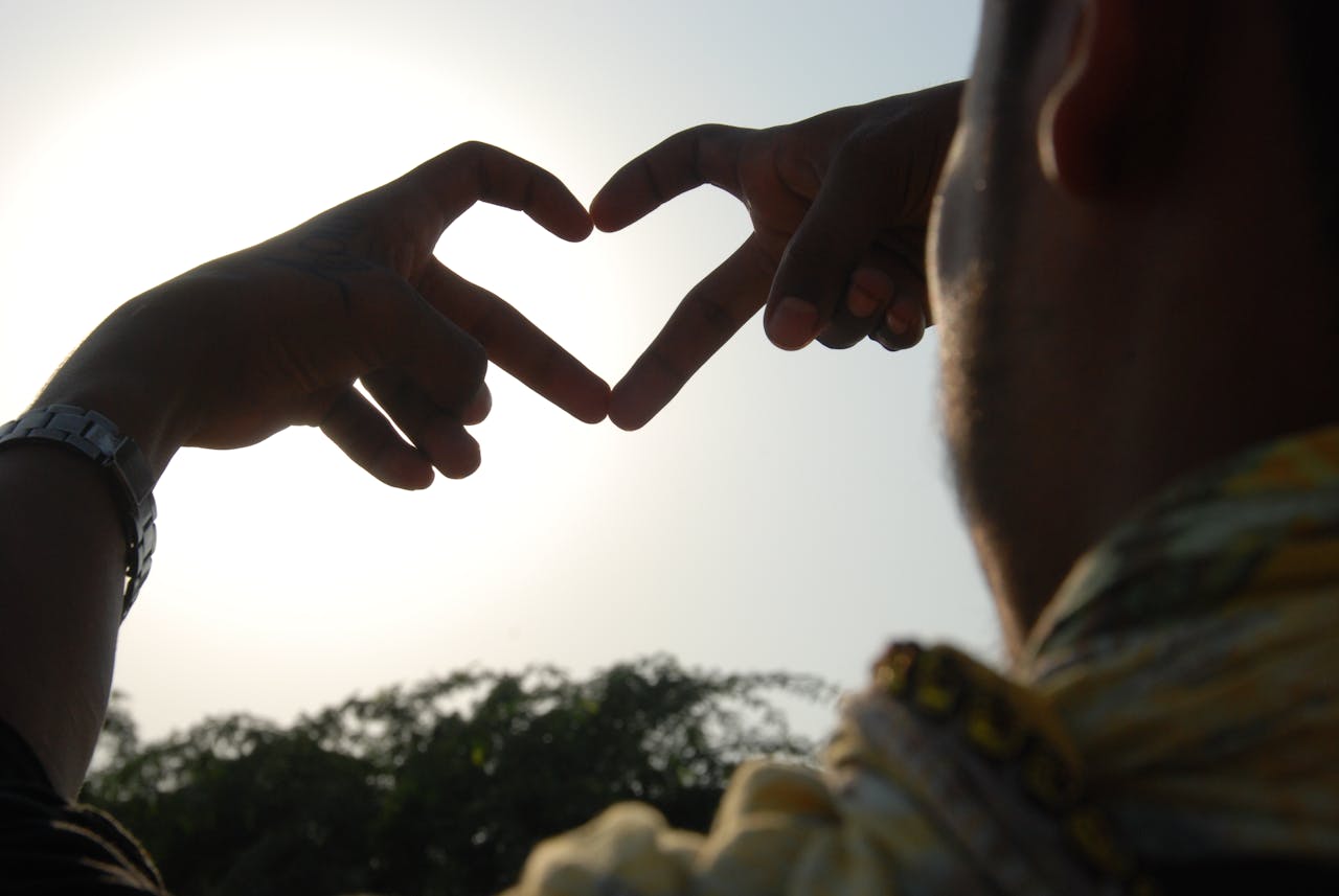 A couple creates a heart shape with their hands against a bright sky, symbolizing love.